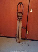 Front view of antique water pump highlighting wooden base and metal handle