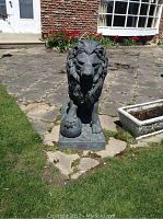 Front view of seated lion statue showing detailed mane and front paw resting on sphere