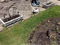 Photo showing two rectangular concrete planters with decorative swirled vine patterns, some wear and outdoor soil residue, placed next to a patch of grass and pavement.