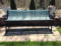 Front view of the green synthetic wood slat bench with black metal frame and armrests on a paved patio.