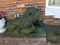 Front profile of green patinated lion and cub sculpture on rectangular base against brick wall