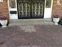 Pair of white cement urns placed outside a brick house entrance on a patio made of stone tiles.