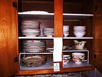 Wooden cabinet shelf with stacks of dinner plates, dessert plates, cereal bowls and gravy boat