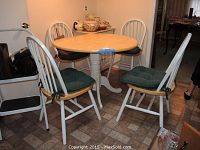 Full view of round wooden kitchen table with four white spindle-back chairs, all with green cushions.