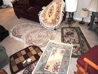 Photo of five throw rugs and welcome mats arranged on a carpeted floor near furniture, showing various shapes and floral patterns as well as a checkered mat