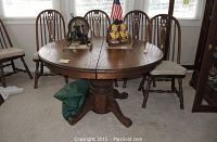 Full side view of round oak table with chairs around and decorative items on top.