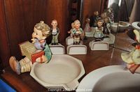 Several Goebel Hummel figurines grouped together on a shelf, showing front view of figurine holding accordion and bird, and others in background