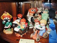 Group view on wooden shelf showing six child figurines and one cat figurine