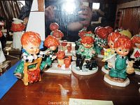 Front view of six red-haired child figurines including child on crutches with cat, child holding flowers, and child with jar.