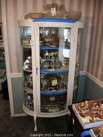 Glass front vintage painted china cabinet shown full of contents but not included in sale. Cabinet has curved glass door, floral painted details and blue protective top cover.