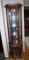 Full view of the tall wooden curio cabinet with glass front and side panels, standing against a wall in a living room space.
