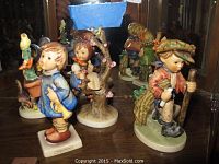Photo of five colorful Goebel Hummel porcelain figurines displayed inside a wooden cabinet with mirrored back.