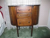 Front view of closed sewing cabinet, three inlaid drawers and curved side panels
