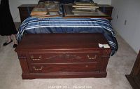 Full closed view of the wooden cedar chest showing carved decorative front panels, brass handles, and wood finish