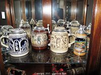 Front and side view of four 6-inch Gerz steins with pewter lids inside a glass cabinet.