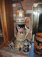 Photo of four Original King beer steins, including a very large 31 inch stein with German inscriptions, a 12 liter stein, and two smaller steins with metal lids and floral designs.
