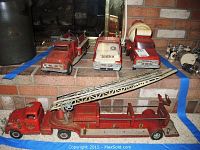 Front view of four red metal toy trucks: fire truck with ladder, small fire truck, fire hose truck, and cement mixer.