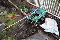 Wide view of garden cart loaded with rake, broom, shepard hooks, bag of mulch, and surrounding garden dirt area