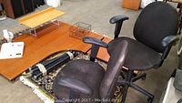 Photo of two black office chairs and the top surface of the wood desk with a small shelf and some folded legs.