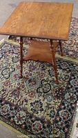 Front view of the antique spindle style table showing the solid oak top, turned legs, and base panel on a patterned rug.