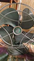 Close-up of green Cool Spot branded fan with metal blades and wire protective cage.