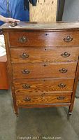 Front view of the antique oak dresser showing five drawers, metal handles, and visible wood grain; some wear and damage visible.