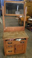 Full view of the antique wooden wash basin stand showing the mirror on top, three drawers, and cupboard below, with visible wear and scratches.