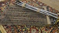 Photo of metal shelving unit parts stacked and bundled on patterned rug showing wire mesh shelves and tubular poles.