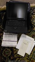 IBM ThinkPad laptop open with screen and keyboard visible, papers/manuals placed in front.