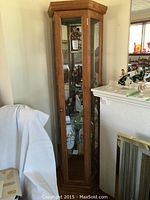Front view of the tall narrow corner curio cabinet with glass door and four glass shelves inside containing decorative items.