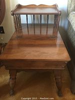 Front view of one wooden end table showing polished colonial style top with turned legs and small back rail.