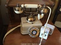 Front view showing overall design of rotary dial phone with cream body, gold dial, and handset resting on cradle.