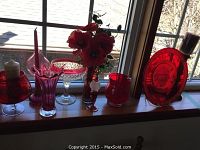 Window ledge display of red glass decor items, including tulip vase, candle holders, plate, flower vase with artificial flowers