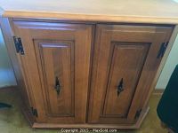 Front view of maple cabinet with two paneled doors, black metal hardware, and beveled edges on top.