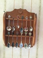 First wooden spoon rack holding 14 souvenir spoons with varied designs such as shell shapes, crests, and floral elements.