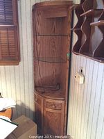 Full view of the light wood corner shelf showing glass shelves and cabinet doors.
