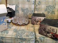 Photo showing assorted crystal glasses including some in original boxes placed on a floral patterned sofa.