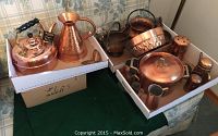 Overview of assorted copper items arranged in two boxes on a couch