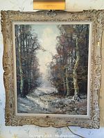 Full view of framed oil painting of winter forest path and accent light above frame