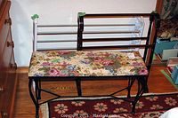 Wrought iron bench with floral upholstered seat and two blanket racks behind it against a wall.
