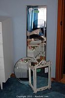 Lot of three mirrors: tall etched mirror, round floral mirror, and three-panel ornate framed mirror stacked on floor.