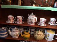 Full view of two shelves with multiple teapots, cups, saucers, and jug in various floral and striped patterns.