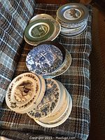 Photo showing stacks of decorative plates with various scenic and historic designs including detailed buildings, landscapes, and traditional border patterns placed on fabric.