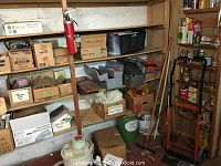 Shelving with various cardboard boxes containing labeled hardware items and extension cords, shop vacuum and dolly on floor.