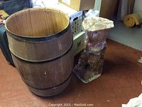 Wide view showing large wooden barrel with dark metal bands and adjacent cement statue mold with natural appearance.