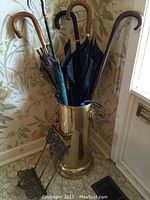 Front view of brass umbrella stand containing umbrellas and canes