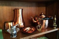 Full view of the copper and brass items arranged on wooden shelf