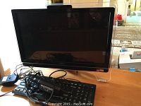 Front view of all-in-one desktop computer with keyboard and cables on wooden table