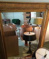 Full view of the rectangular mirror showing wooden gold ornate frame and clear mirror reflecting surrounding lamps and boxes.