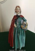 Front view of Royal Doulton 'Jean' porcelain figurine, showing the woman with red hooded cape, green dress, and flower basket.